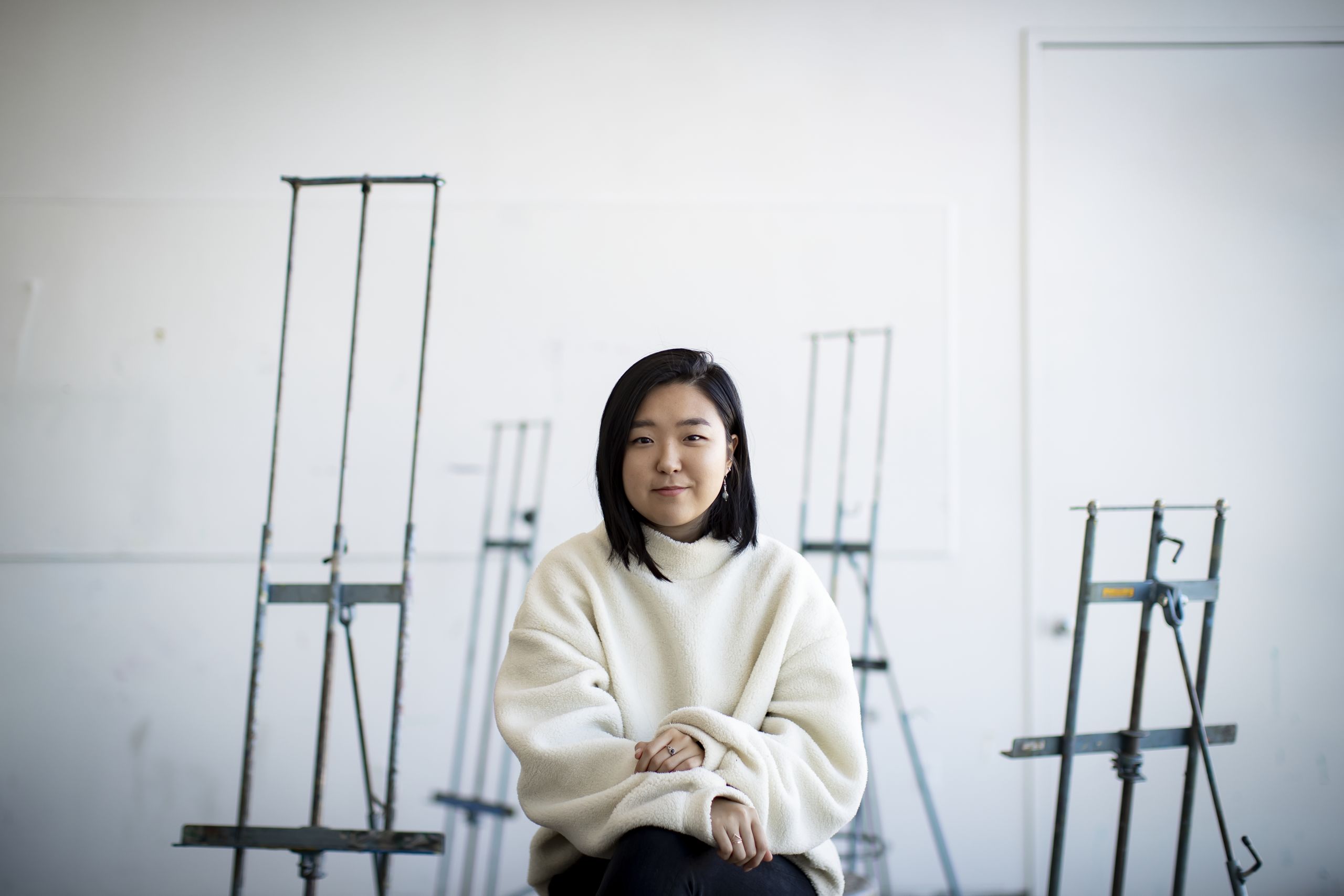 Ye Jin Jeon sitting in a bright art studio surrounded by easels. 