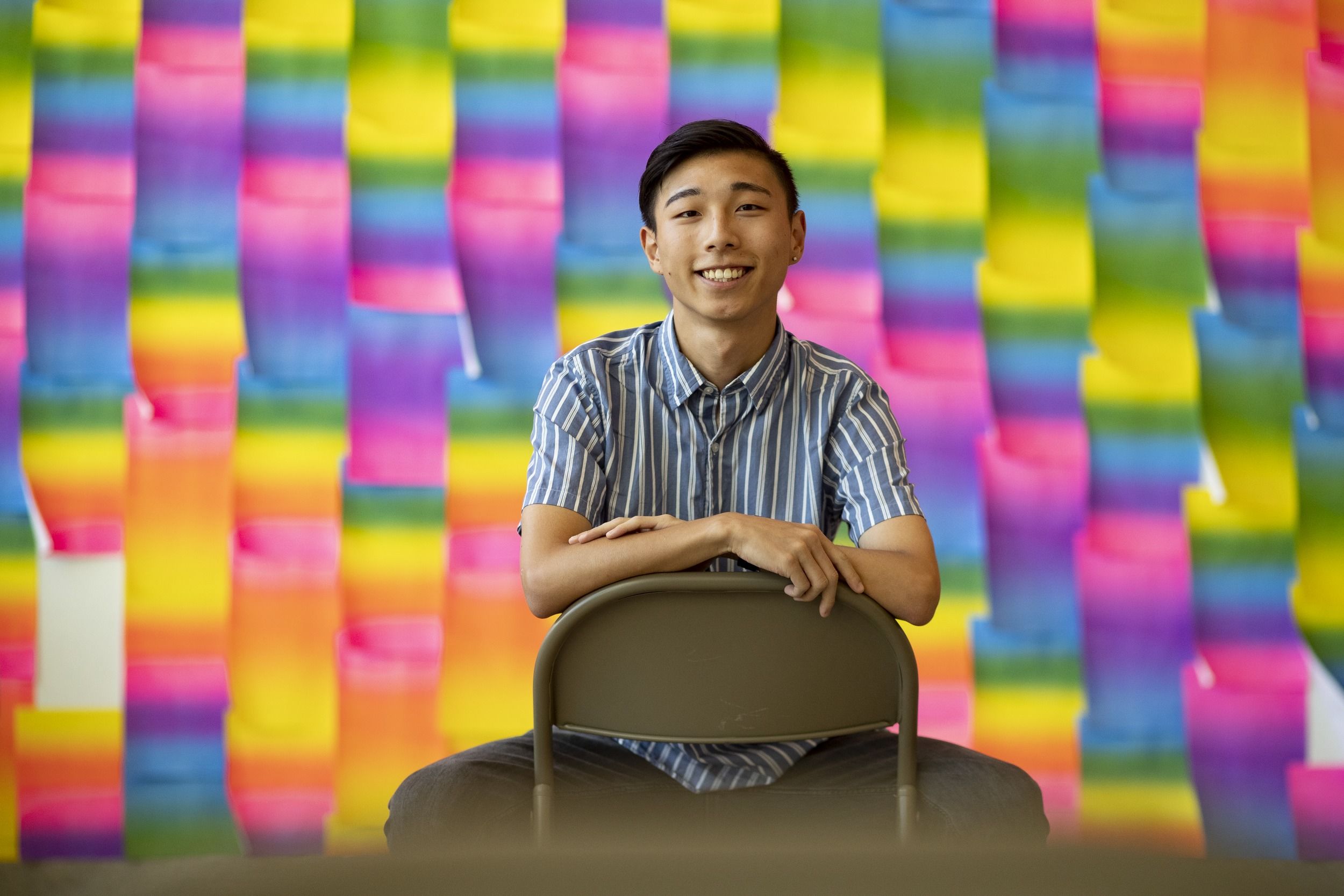 Xinjian Li sitting in front of a colorful art installation at the Tyler School of Art and Architecture. 