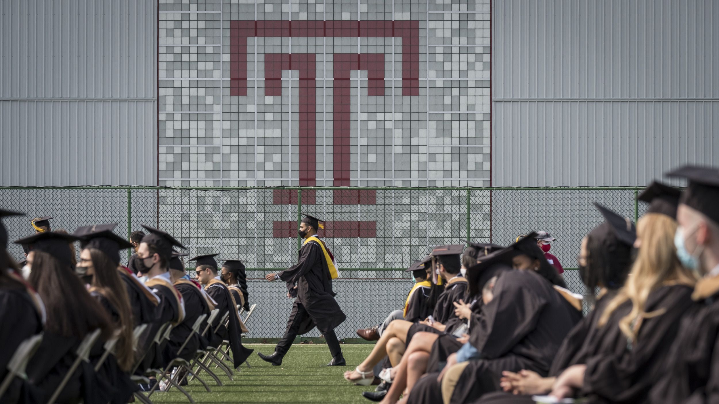 Graduates walking across the Edberg-Olson field in front of a Temple "T."