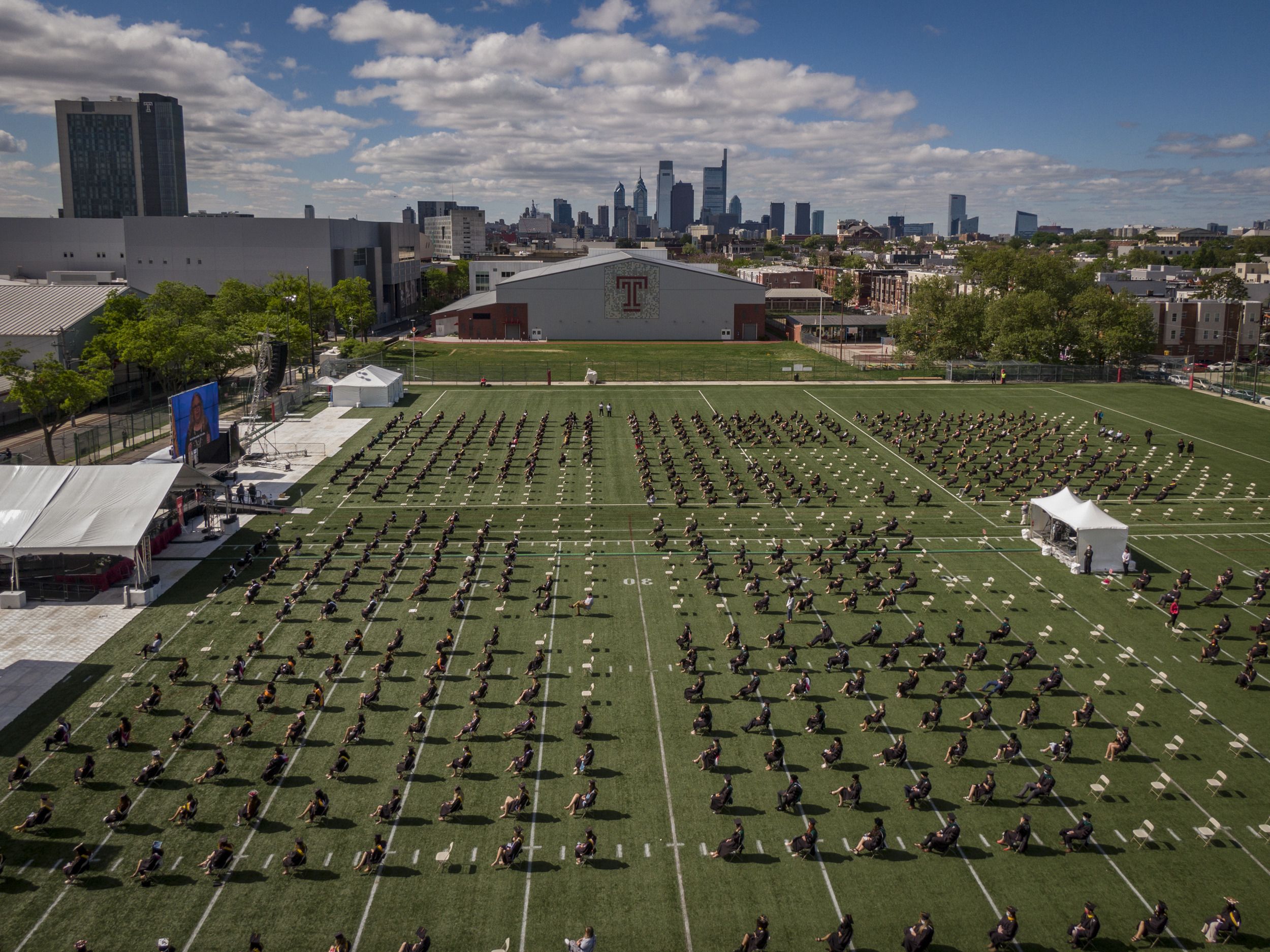 Graduates sitting on the field at Edberg-Olson Athletic Hall with the Philadelphia skyline in the background.