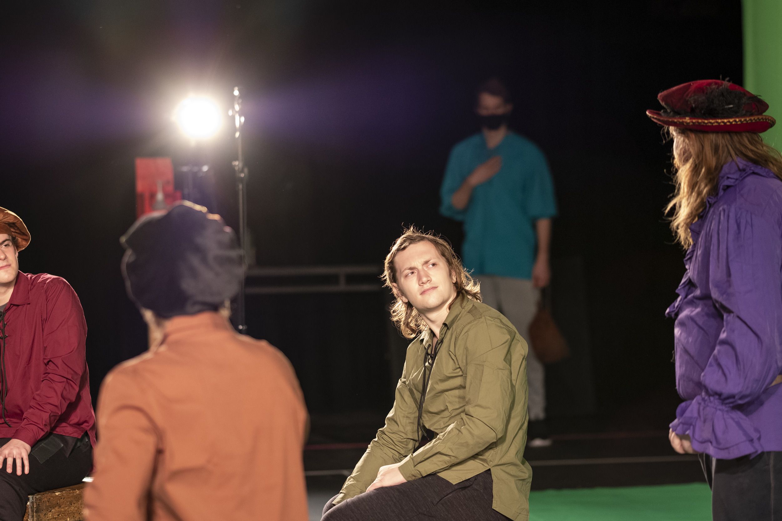 An actor in a moss green shirt looks up at another actor.