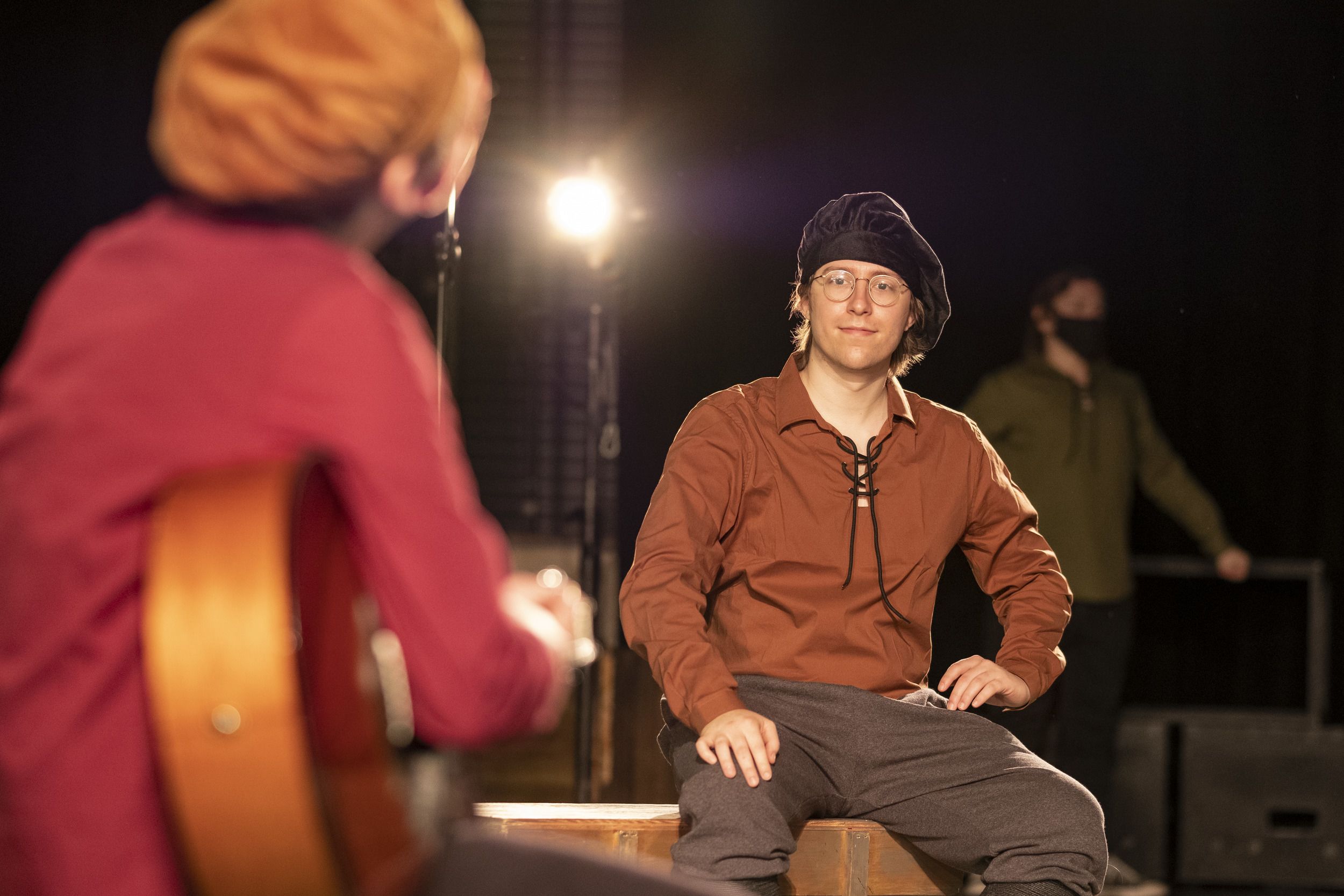 An actor in a brown shirt and black beret smiles for the camera.